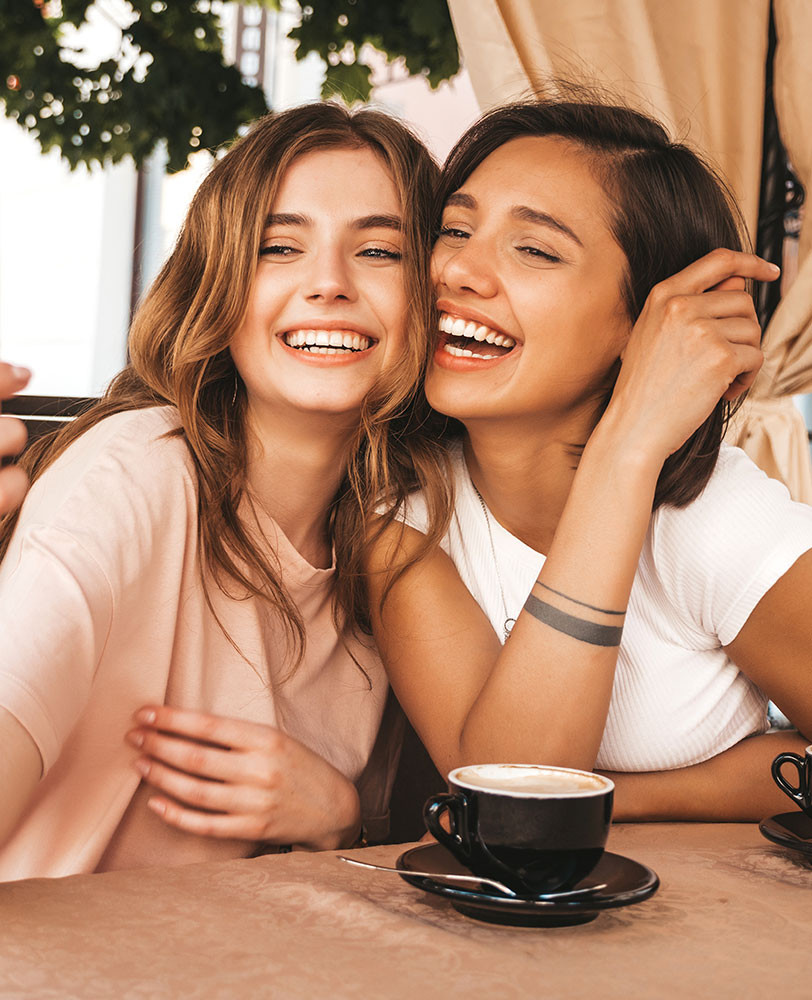 2 amigas sac&aacute;ndose una selfie mientras toman un caf&eacute;